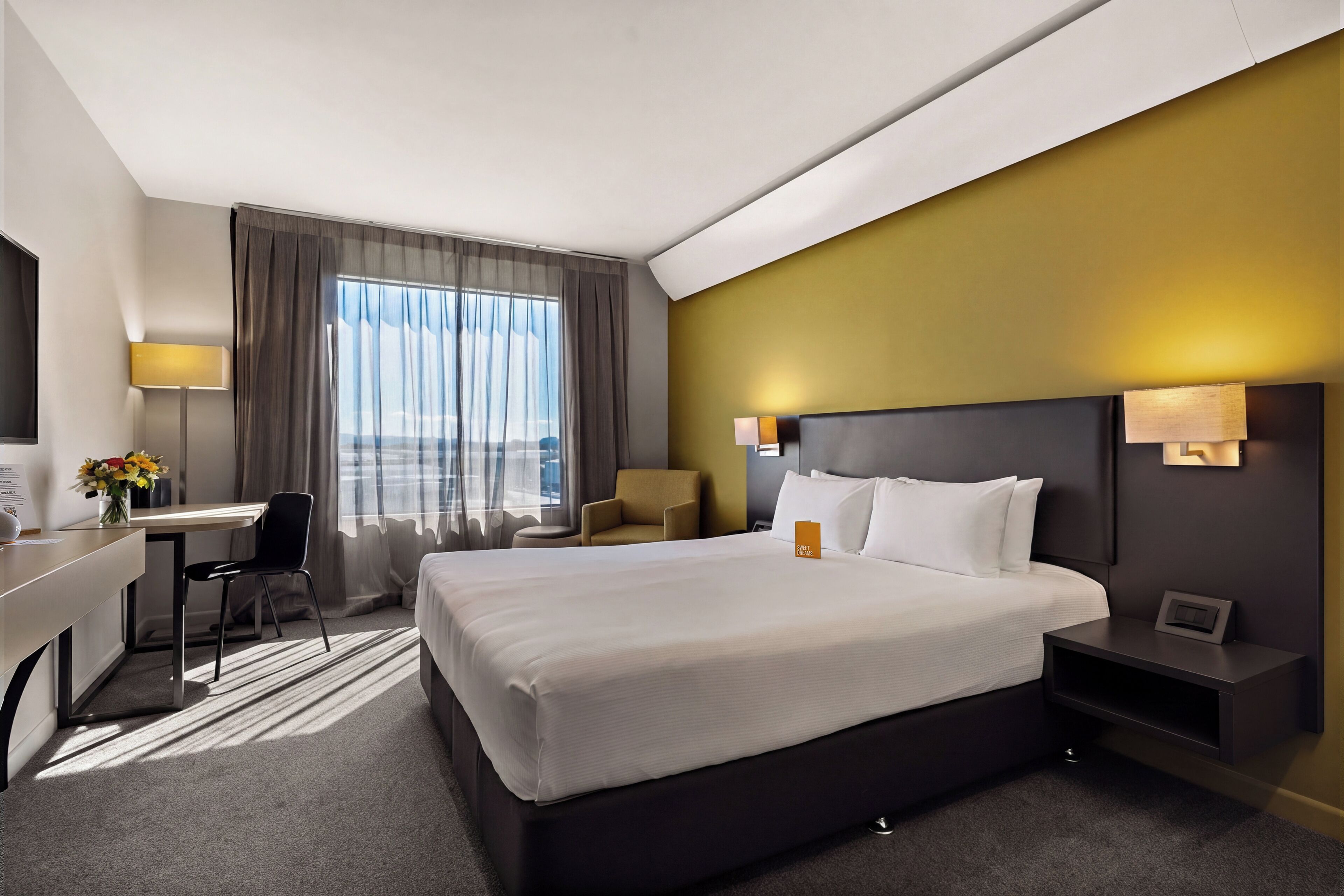 Habitación de hotel con una cama grande, un escritorio, una silla, una lámpara y vistas al exterior.