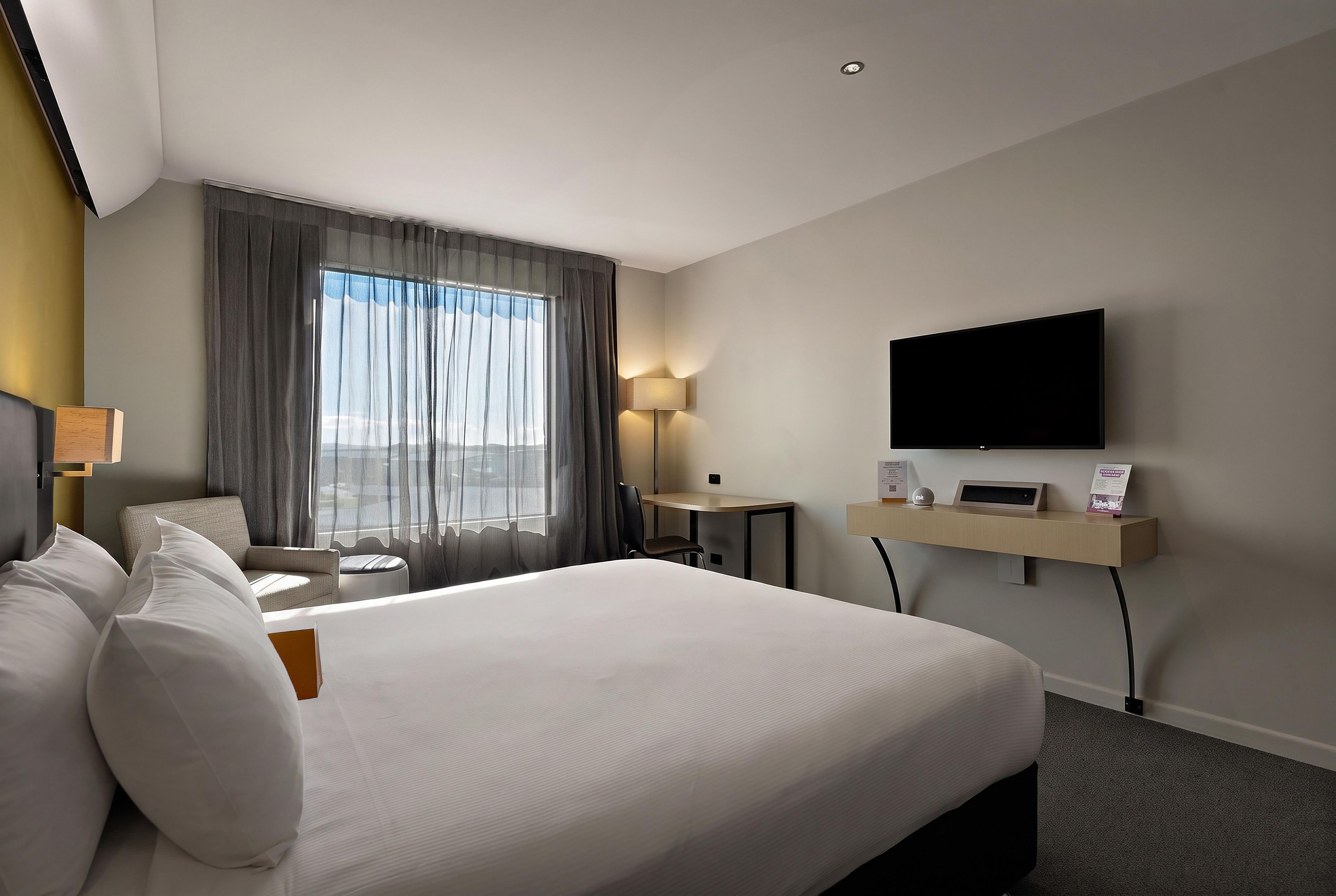 A hotel room with a large bed, a desk, a flat-screen TV, and a window with curtains.