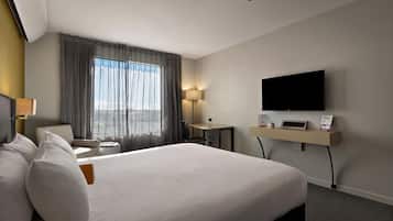A hotel room with a large bed, a desk, a flat-screen TV, and a window with curtains.