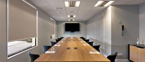 A conference room with a long table, chairs, a flat-screen TV, and a telephone on the wall.