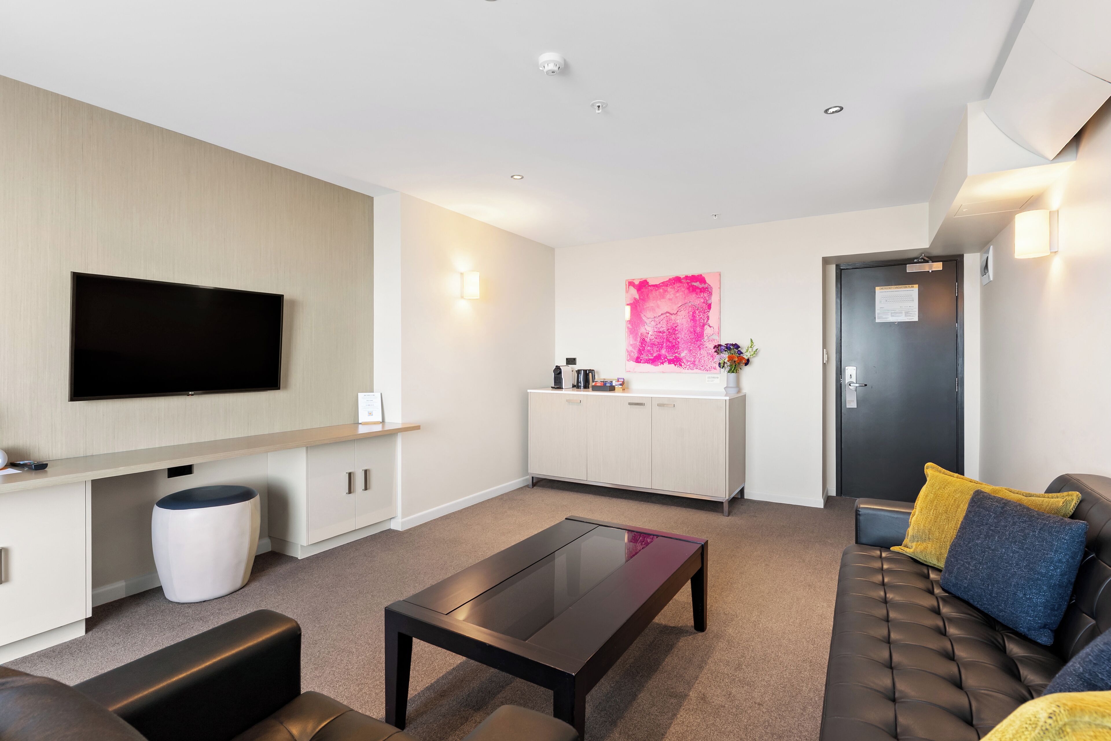 A modern living room with a flat-screen TV, a sofa, a coffee table, and a kitchen area with a sink and cabinets.