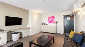 A modern living room with a flat-screen TV, a sofa, a coffee table, and a kitchen area with a sink and cabinets.