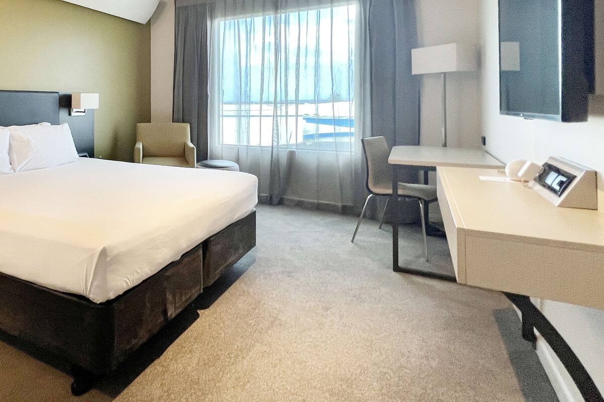 A hotel room with a bed, a desk, a chair, a lamp, and a window with curtains.