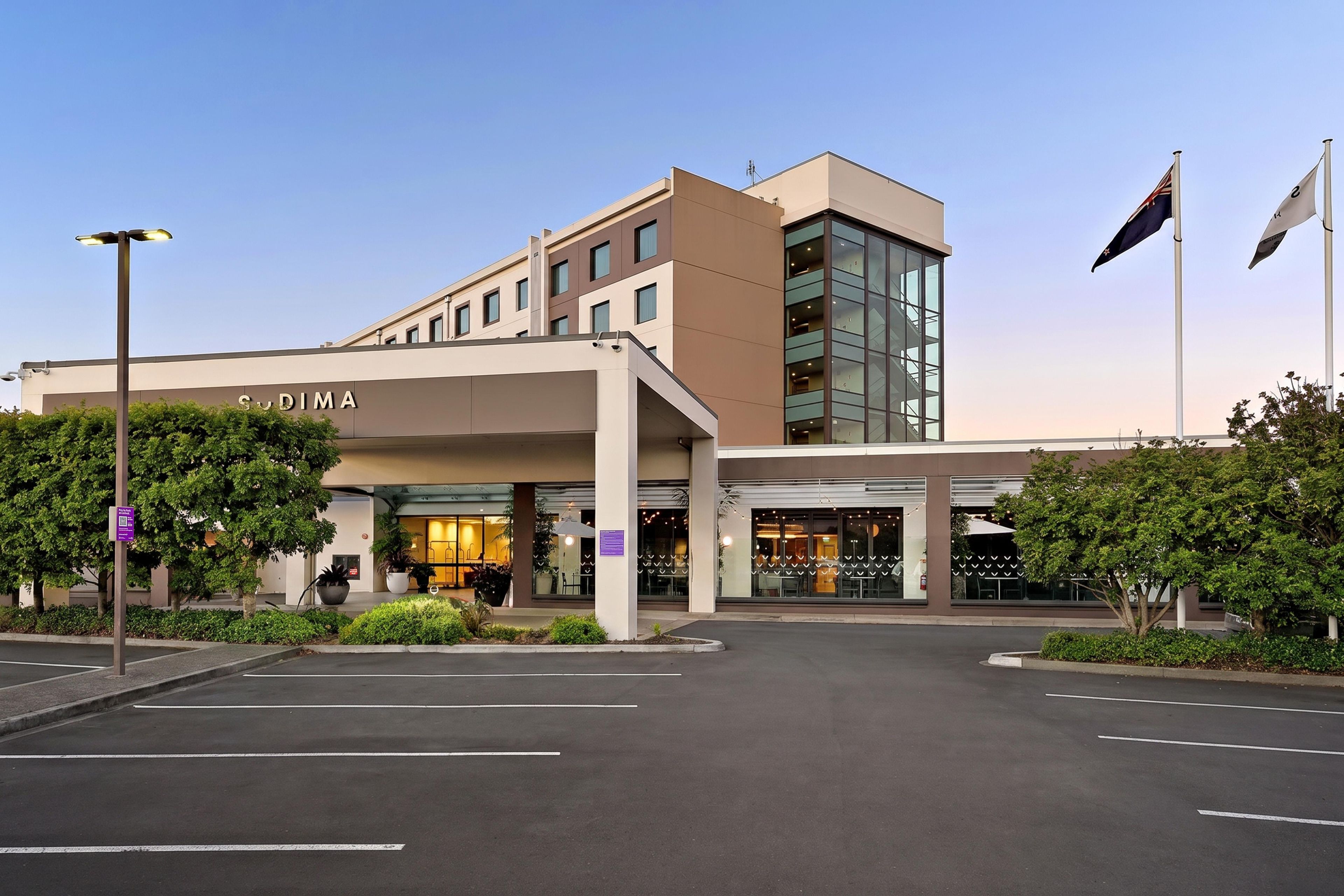 A modern hotel with a clear entrance, a parking lot, and a flag on the right.