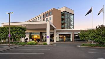 A modern hotel with a clear entrance, a parking lot, and a flag on the right.