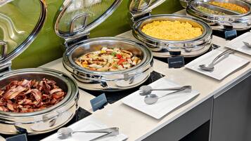 A buffet with various food options including scrambled eggs, chicken sausages, and bacon.