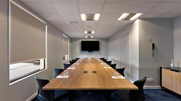 A conference room with a long table, chairs, a flat-screen TV, and a telephone on the wall.