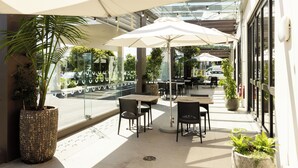 An outdoor cafe with tables and chairs under a glass roof, surrounded by potted plants. - Sudima Auckland Airport (Auckland)