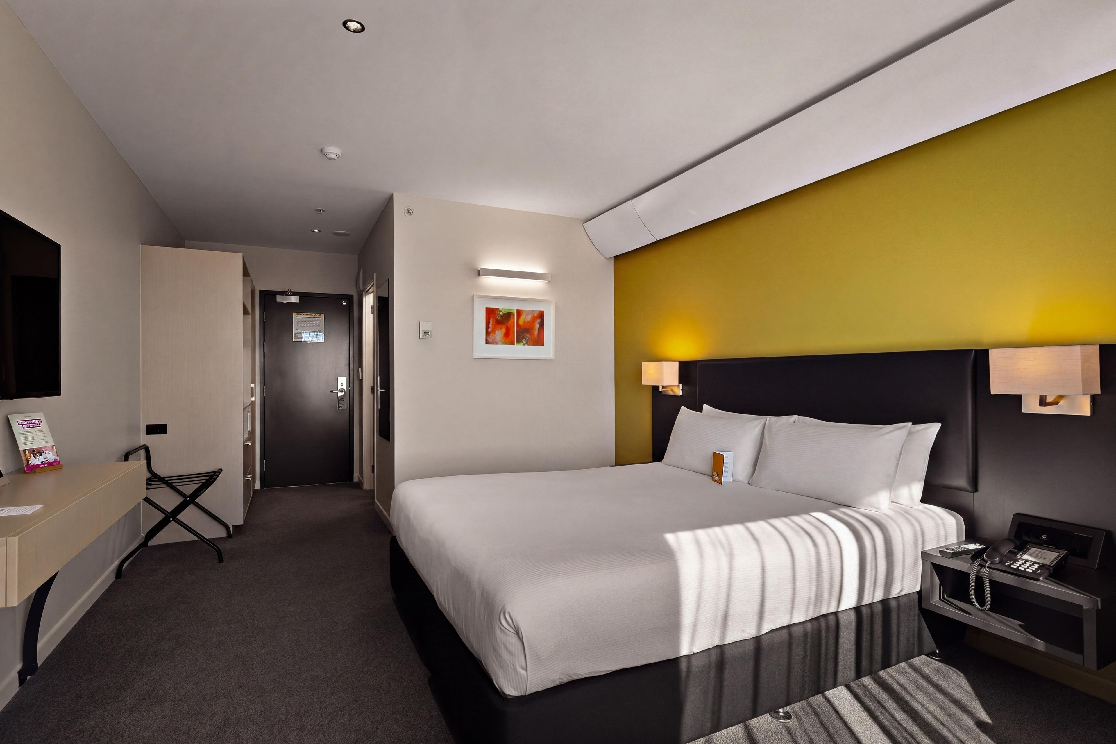 Ein Hotelzimmer mit einem Bett, Nachttischen, einem Schreibtisch, einem Sessel, einem Fernseher und einer Tür.