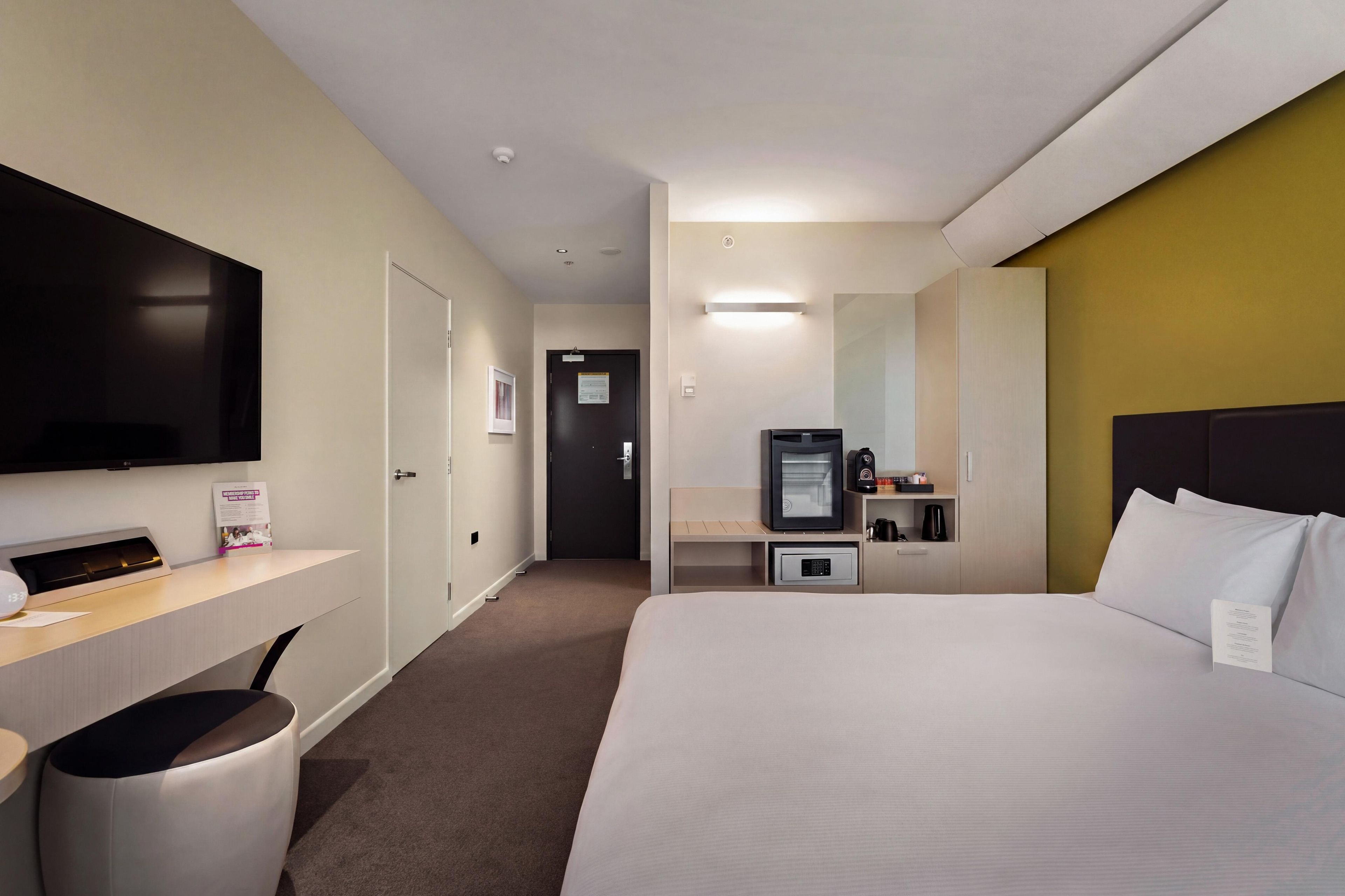 Habitación de hotel con cama, escritorio, televisión de pantalla plana, cafetera y minibar.