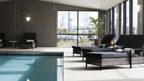 A modern indoor pool area with lounge chairs and a view of the outside. - Sudima Auckland Airport (Auckland)