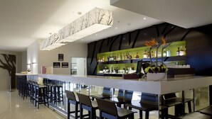 A modern bar area with a long counter, multiple bar stools, and a variety of liquor bottles. - Sudima Auckland Airport (Auckland)