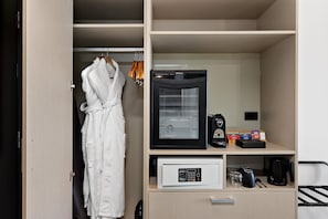 A hotel room with a robe hanging, a coffee machine, and a microwave on the counter.