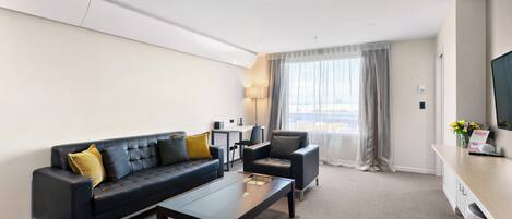 Una habitación de hotel moderna con un sofá de cuero negro, una mesita, una silla y un gran ventanal con cortinas.