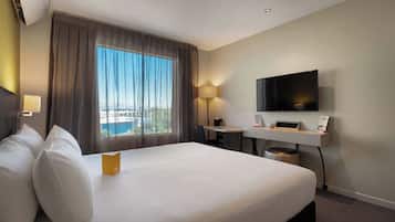 Habitación de hotel con una cama grande, un escritorio, un televisor de pantalla plana, una lámpara y vista a la ciudad desde la ventana.