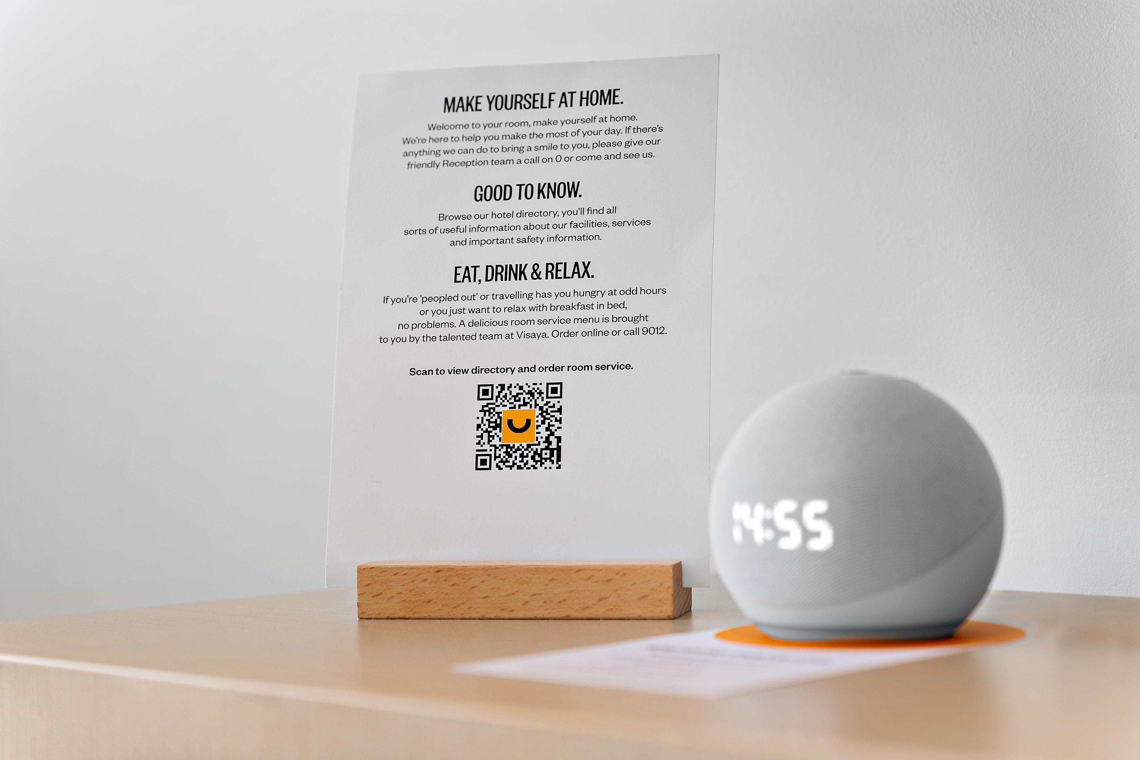 Ett informationskort om hotellet med en QR-kod, en träkloss och ett grått föremål på ett bord.