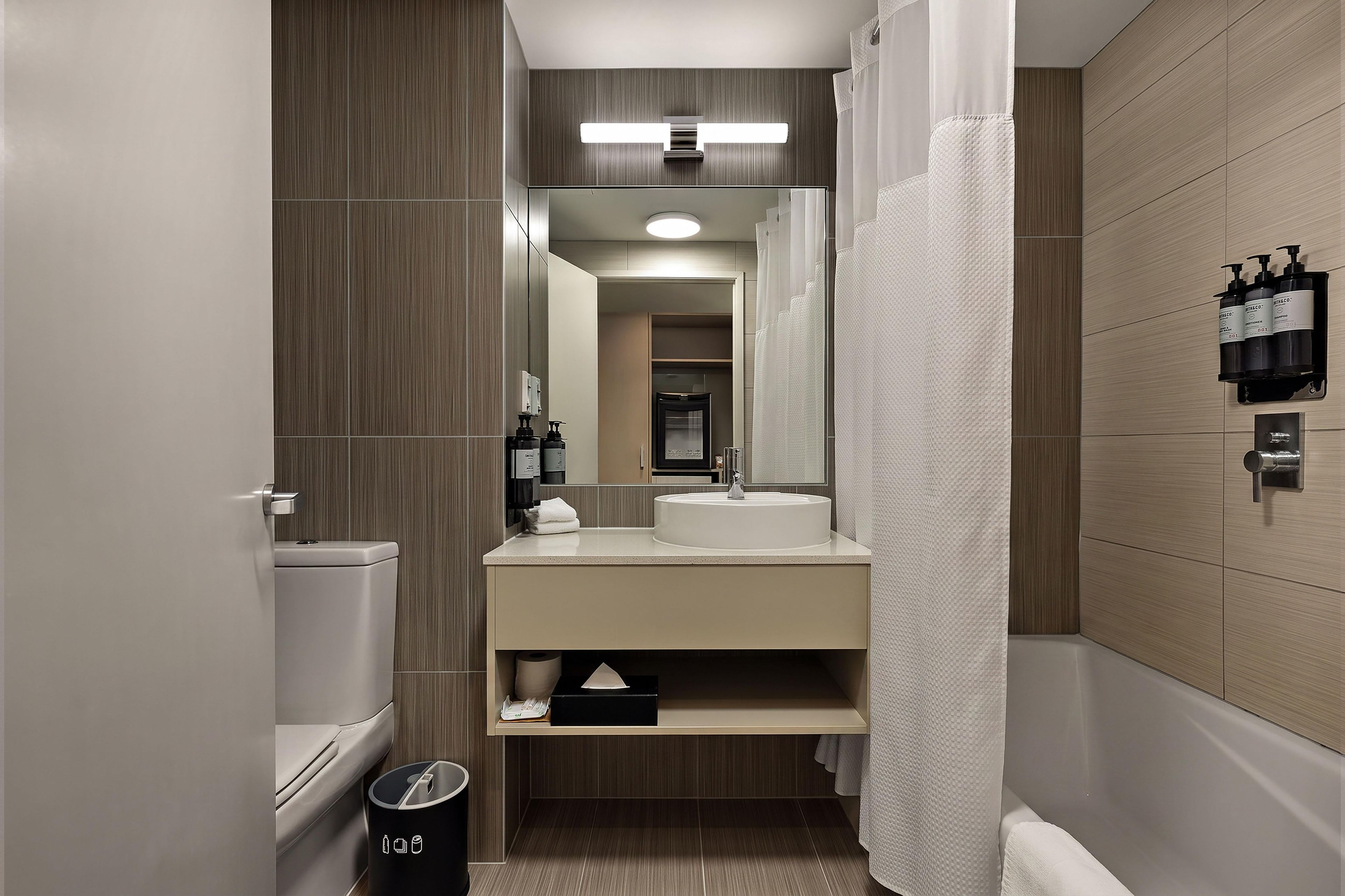 Un baño moderno con inodoro, lavamanos, espejo y cortina de ducha.