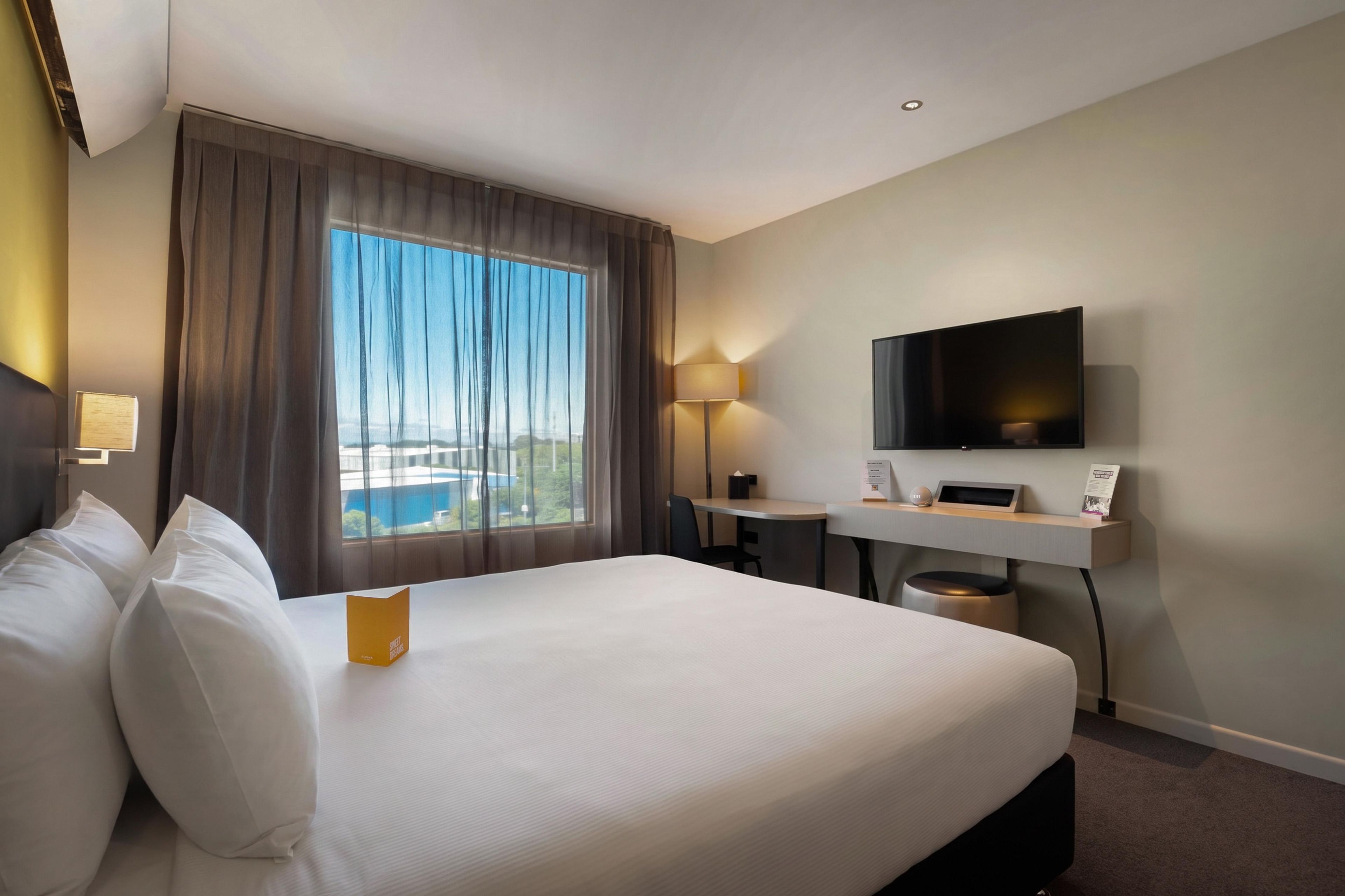 Una habitación de hotel con una cama grande, un escritorio, un televisor y una ventana con cortinas.