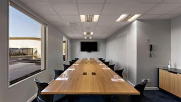 A conference room with a long table, chairs, a flat-screen TV, and a window with a view of a building.