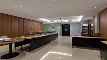 A modern, well-lit room with a long counter for food service, a door labeled 'Pavilion 1,' and a refrigerator stocked with beverages.