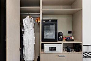 A hotel room with a robe hanging, a coffee machine, and a microwave on the counter.