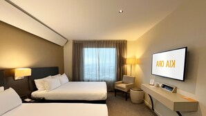 A hotel room with two beds, a TV mounted on the wall, a desk with a lamp, and a view of the outdoors through the window. - Sudima Auckland Airport (Auckland)