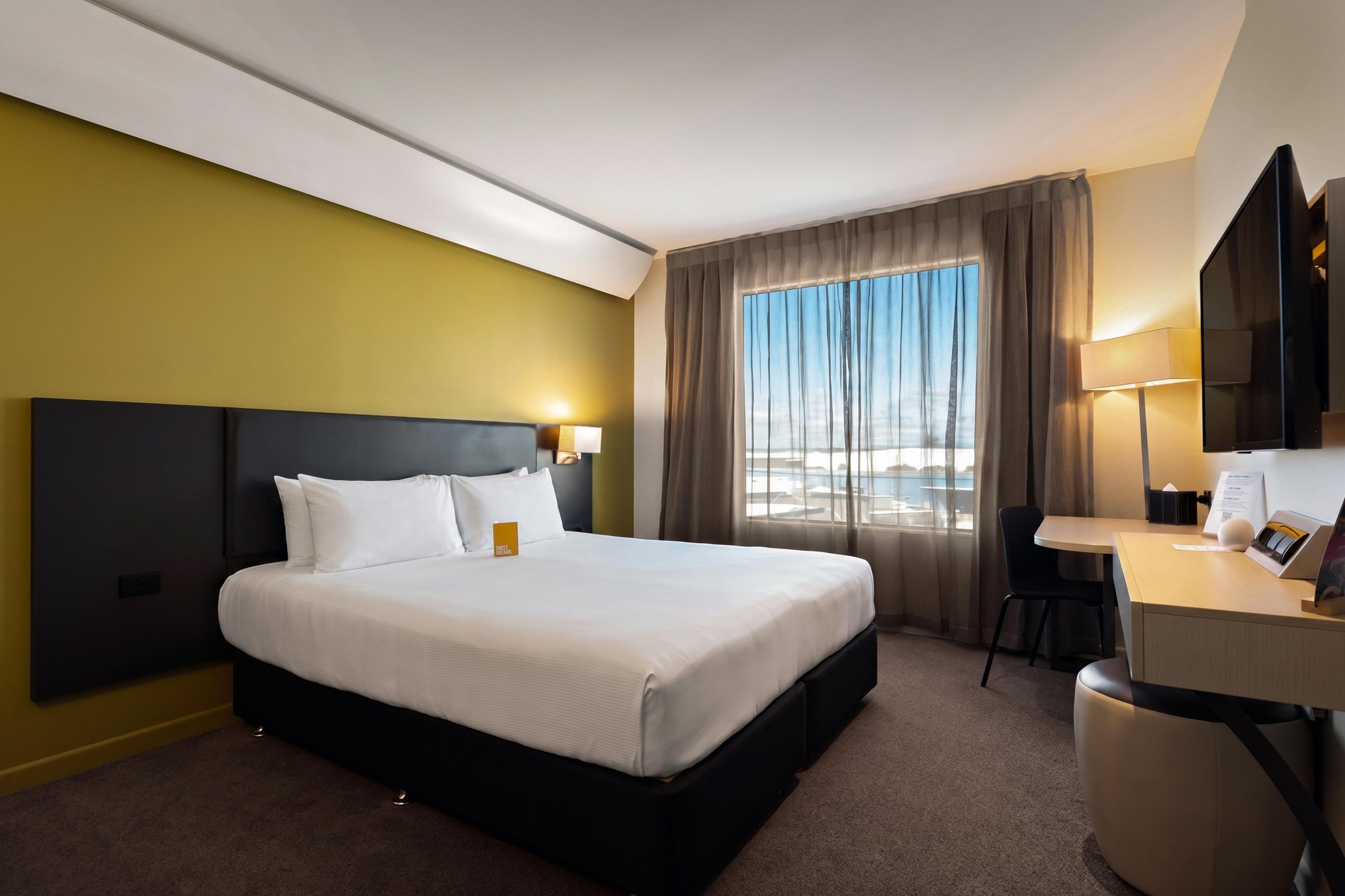 A hotel room with a bed, a desk, a chair, a TV, and a window with curtains.