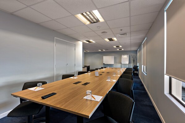 A conference room with a long table, chairs, a projector screen, and a window.