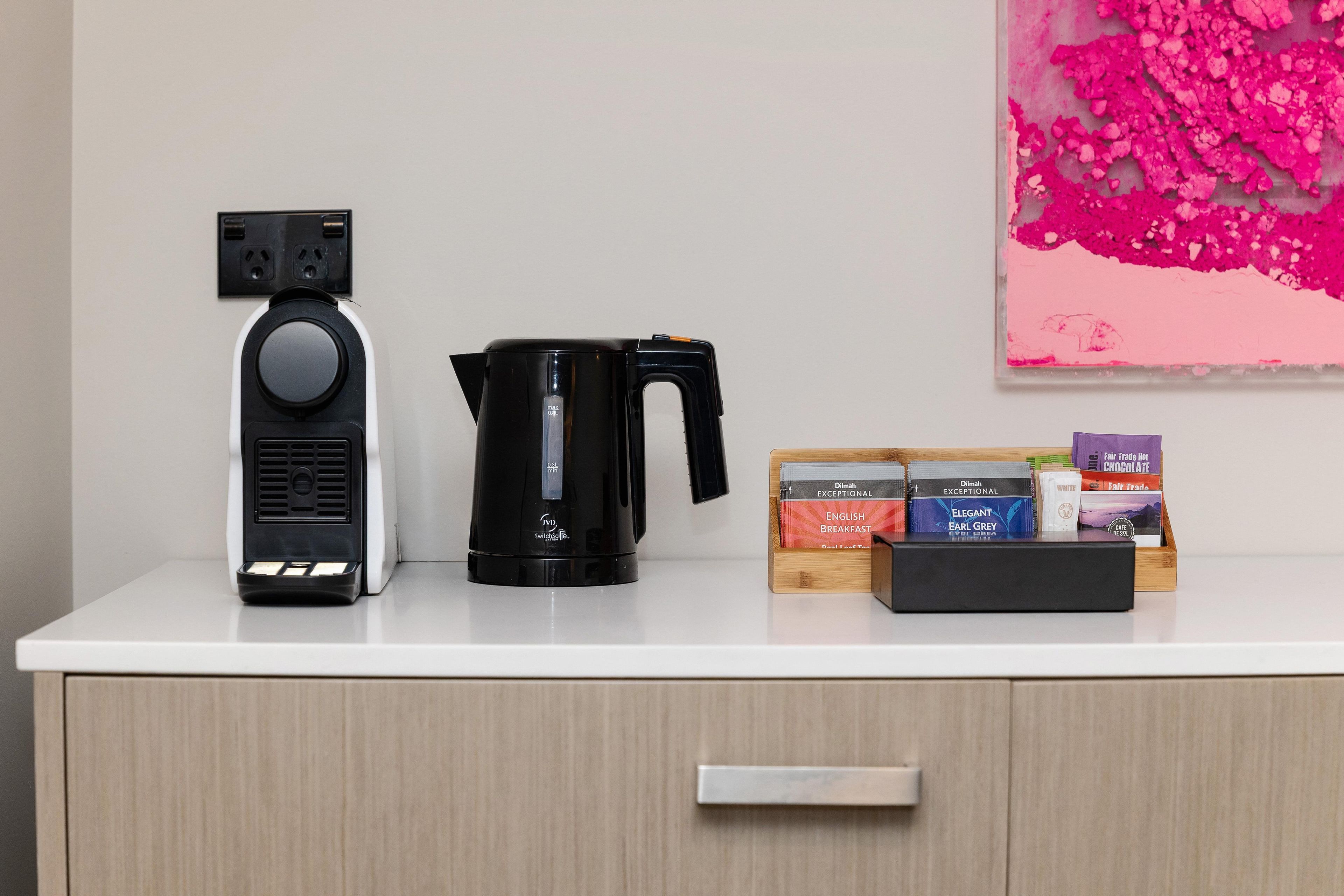 A coffee maker, a kettle, and a box of tea on a white counter.