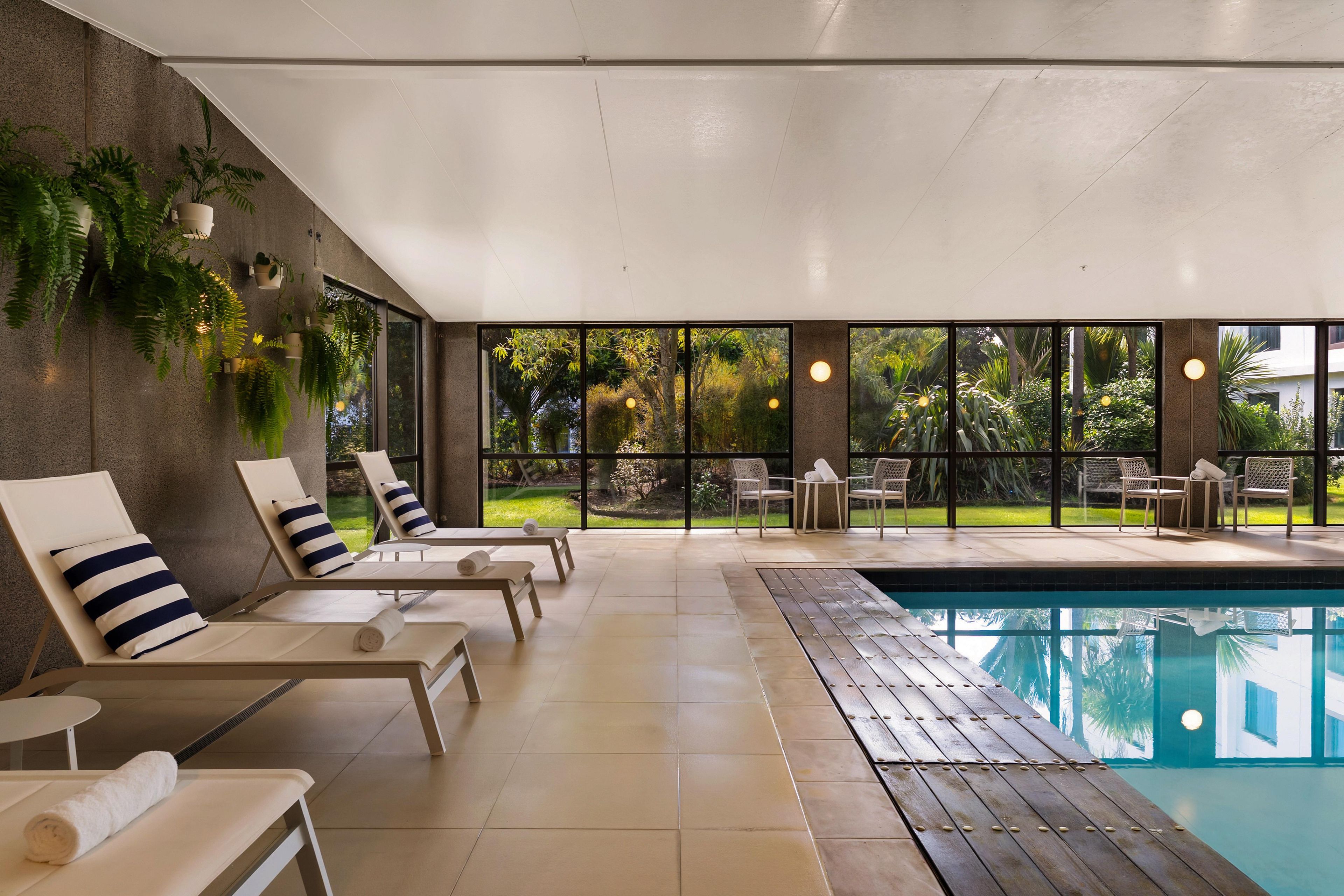 A poolside area with lounge chairs, a pool, and a view of a garden.