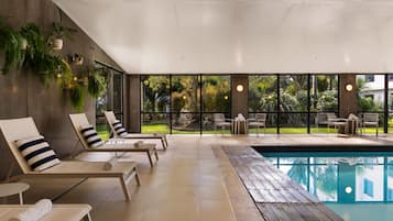 A poolside area with lounge chairs, a pool, and a view of a garden.