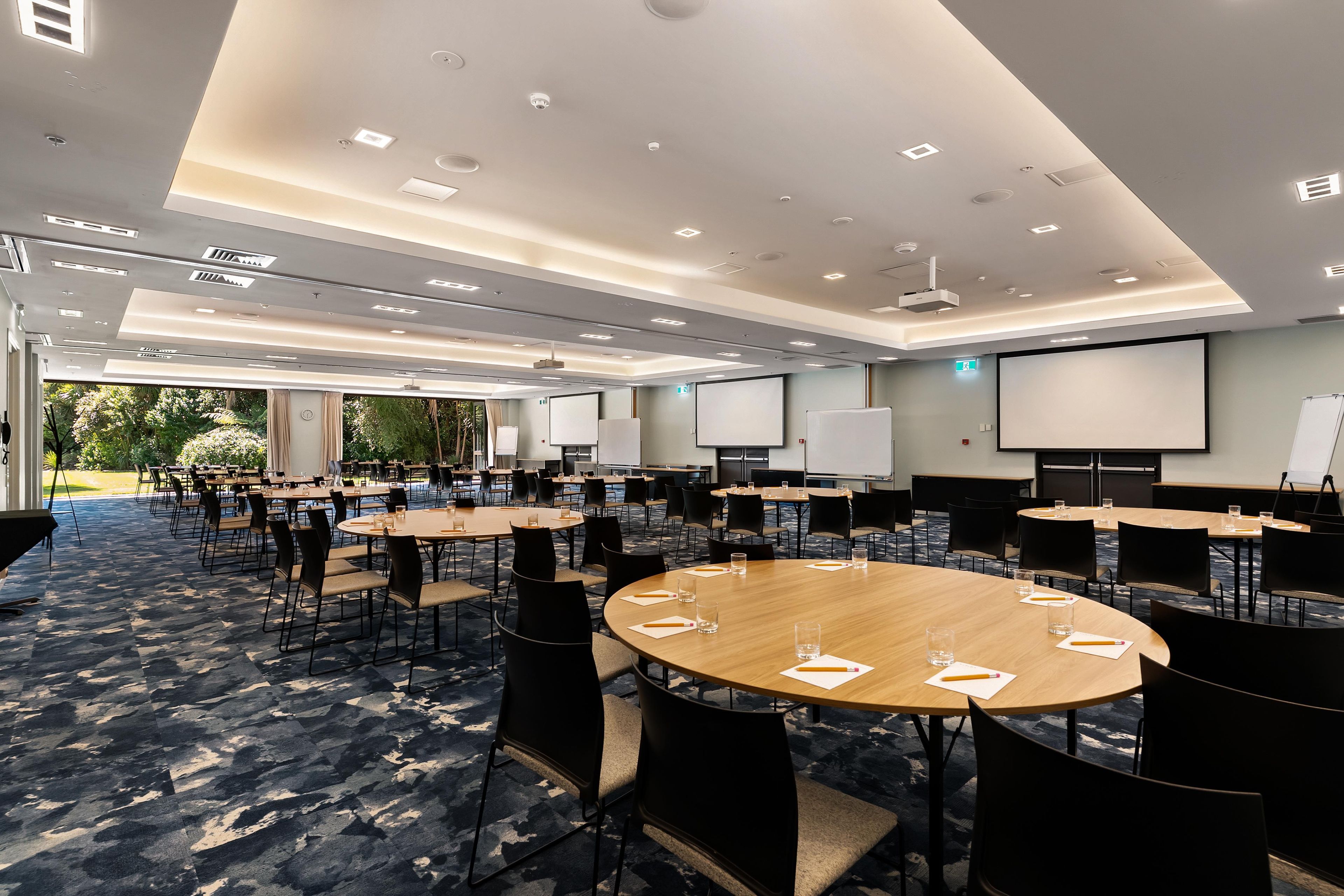 Une salle de conférence équipée de plusieurs tables et chaises, d’un grand écran et d’un projecteur.