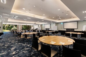 A conference room with multiple tables and chairs, a large screen, and a projector. - Sudima Auckland Airport (Auckland)