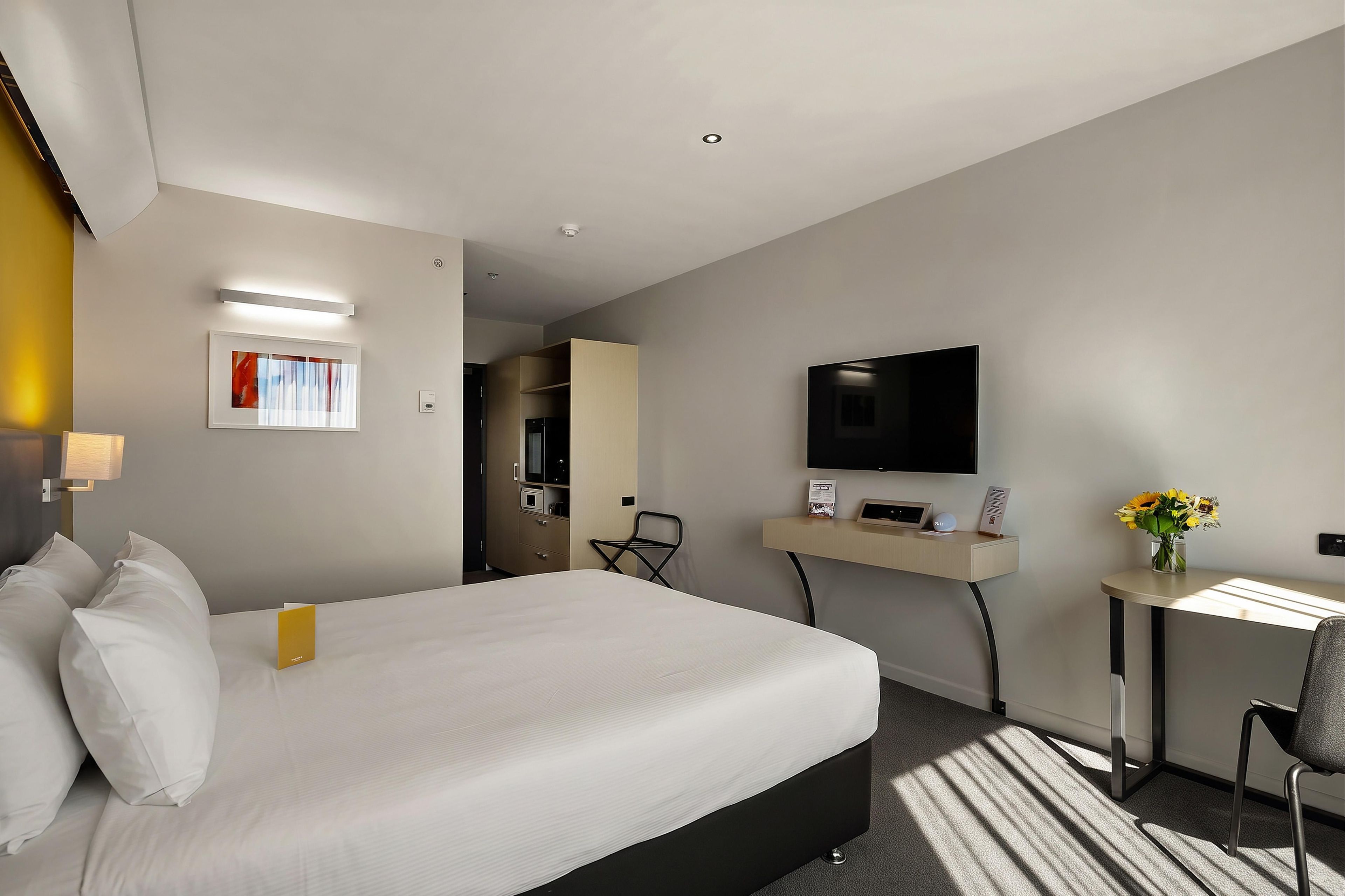 Une chambre d’hôtel avec un lit, un bureau, une chaise, une télévision et une fenêtre.