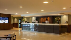A modern hotel reception area with a reception desk, a flat-screen TV, and a seating area with a bench. - Sudima Auckland Airport (Auckland)
