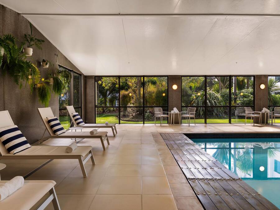 A poolside area with lounge chairs, a pool, and a view of a garden.