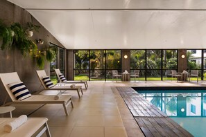 Zona junto a la piscina con sillas de descanso, piscina y vista a un jardín.