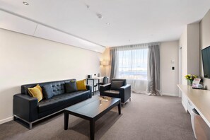 A modern hotel room with a black leather sofa, a coffee table, a desk, and a large window with curtains. - Sudima Auckland Airport (Auckland)