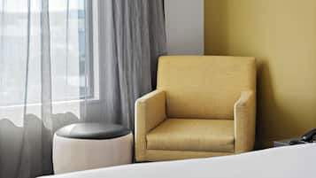 Una habitación de hotel con un sillón individual, un pequeño taburete y una cama.
