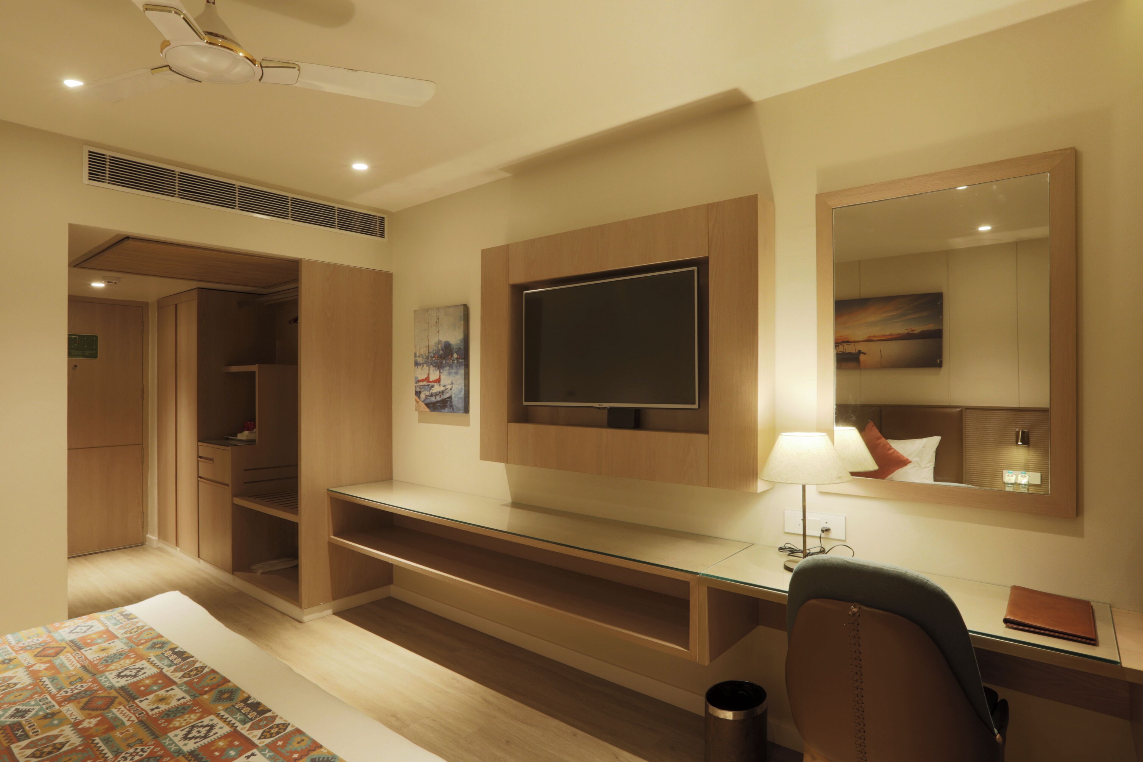 A hotel room with a bed, a desk, a chair, a TV, a mirror, and a wardrobe.