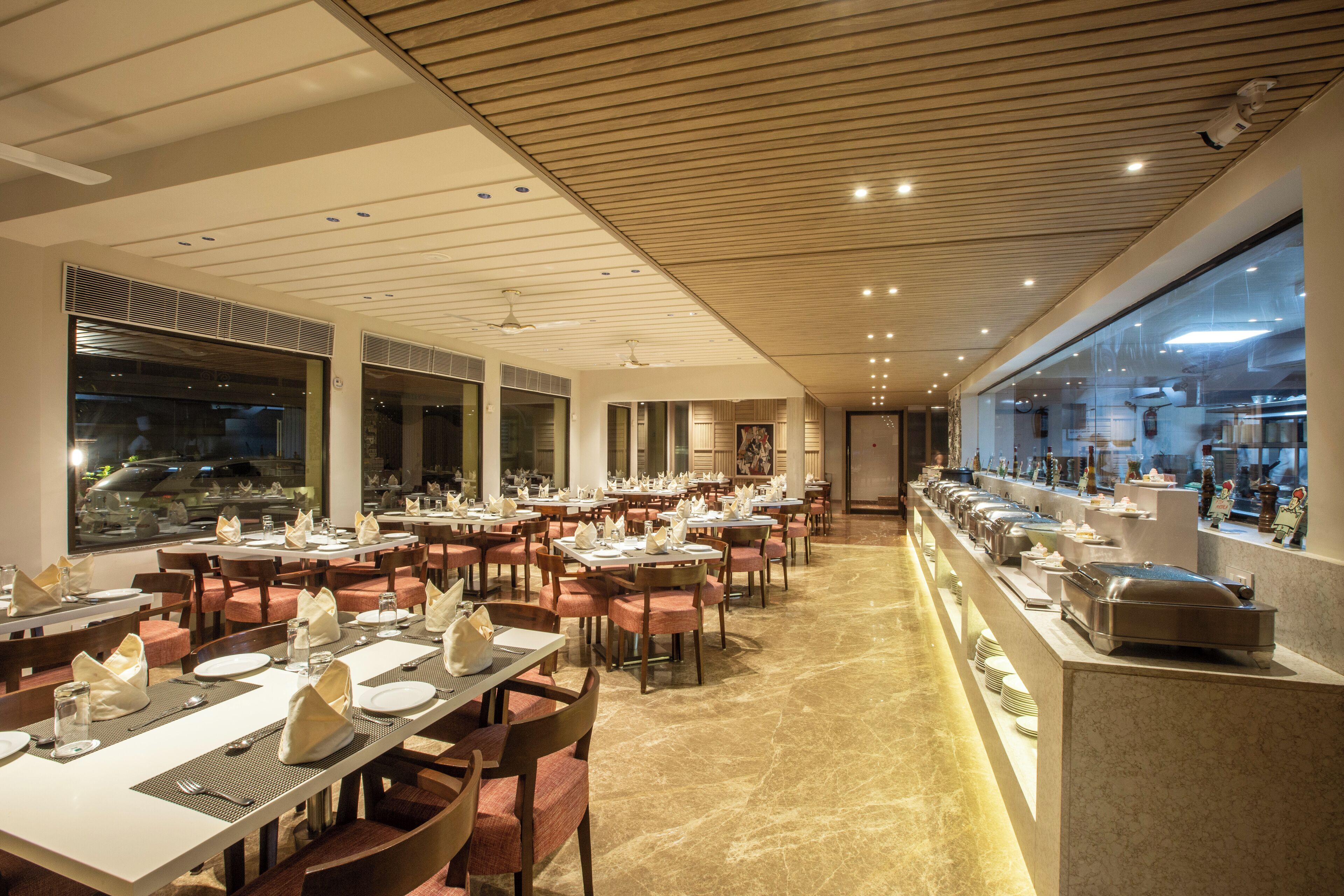 Un restaurant spacieux doté de nombreuses tables et chaises, d’un espace buffet et de grandes fenêtres offrant une vue sur l’extérieur.
