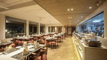 Un restaurant spacieux doté de nombreuses tables et chaises, d’un espace buffet et de grandes fenêtres offrant une vue sur l’extérieur.
