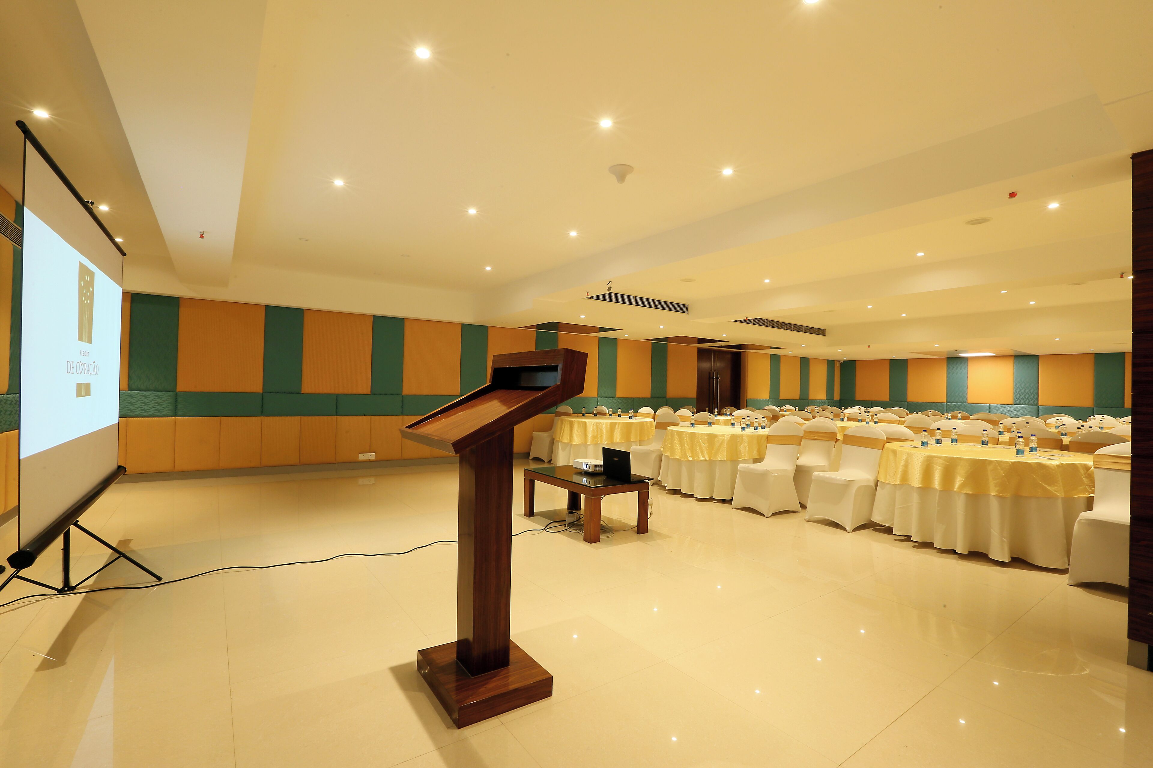 Una sala de conferències amb un escenari, una pantalla de projector i taules preparades per a una reunió.
