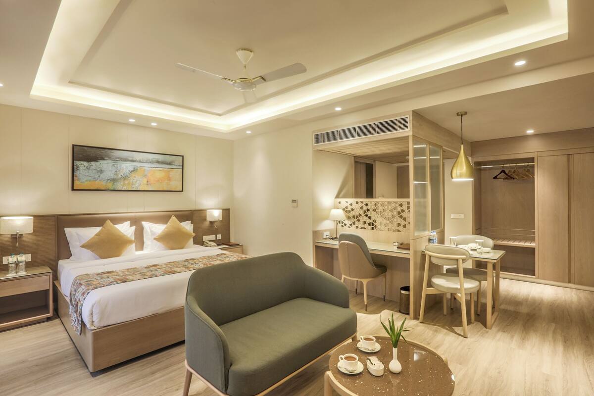 A modern hotel room with a bed, a desk, a chair, a sofa, and a mirror.