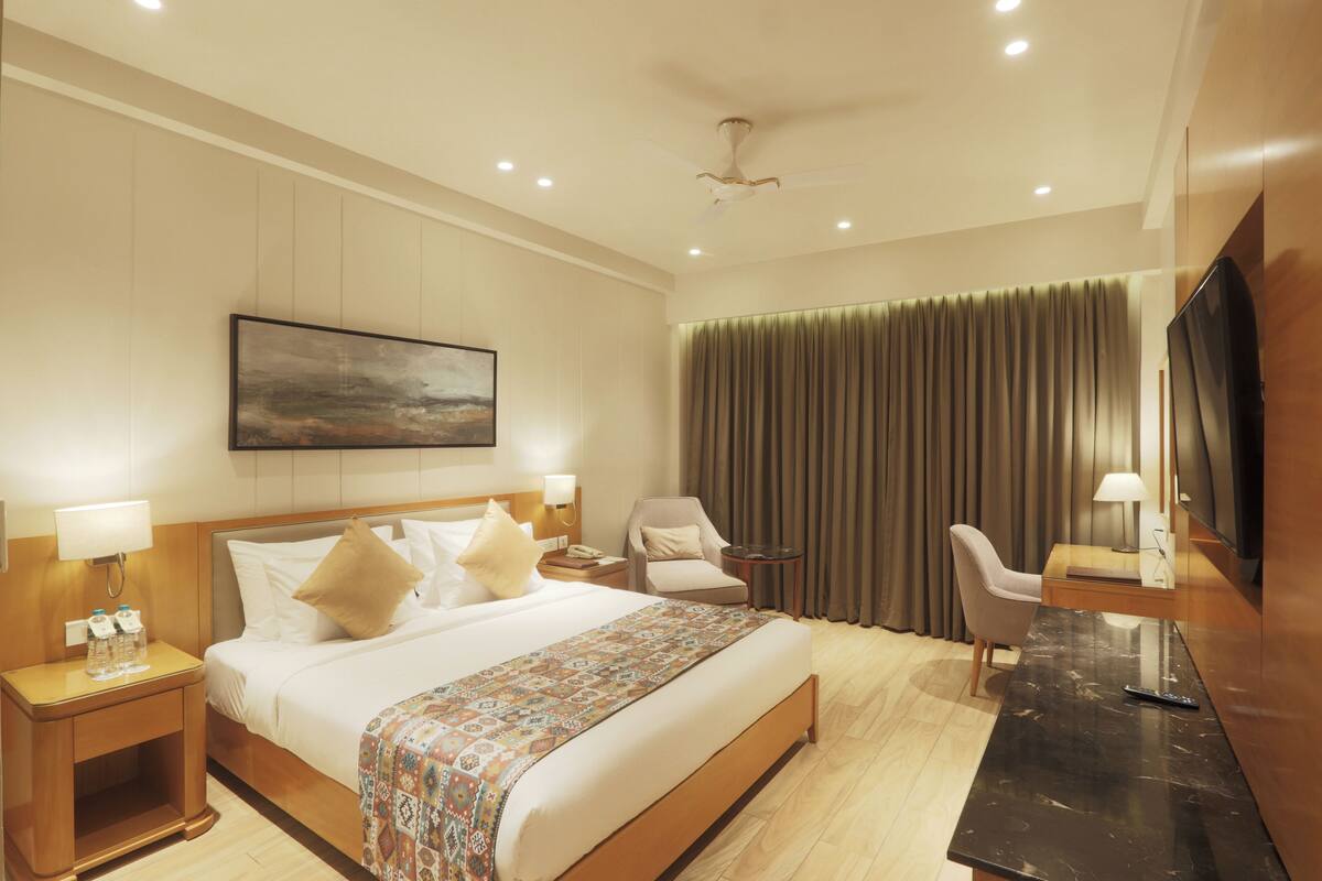 A hotel room with a large bed, a desk, a chair, a TV, and a painting on the wall.
