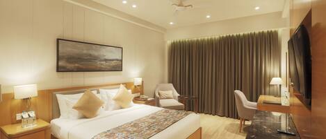A hotel room with a large bed, a desk, a chair, a TV, and a painting on the wall.