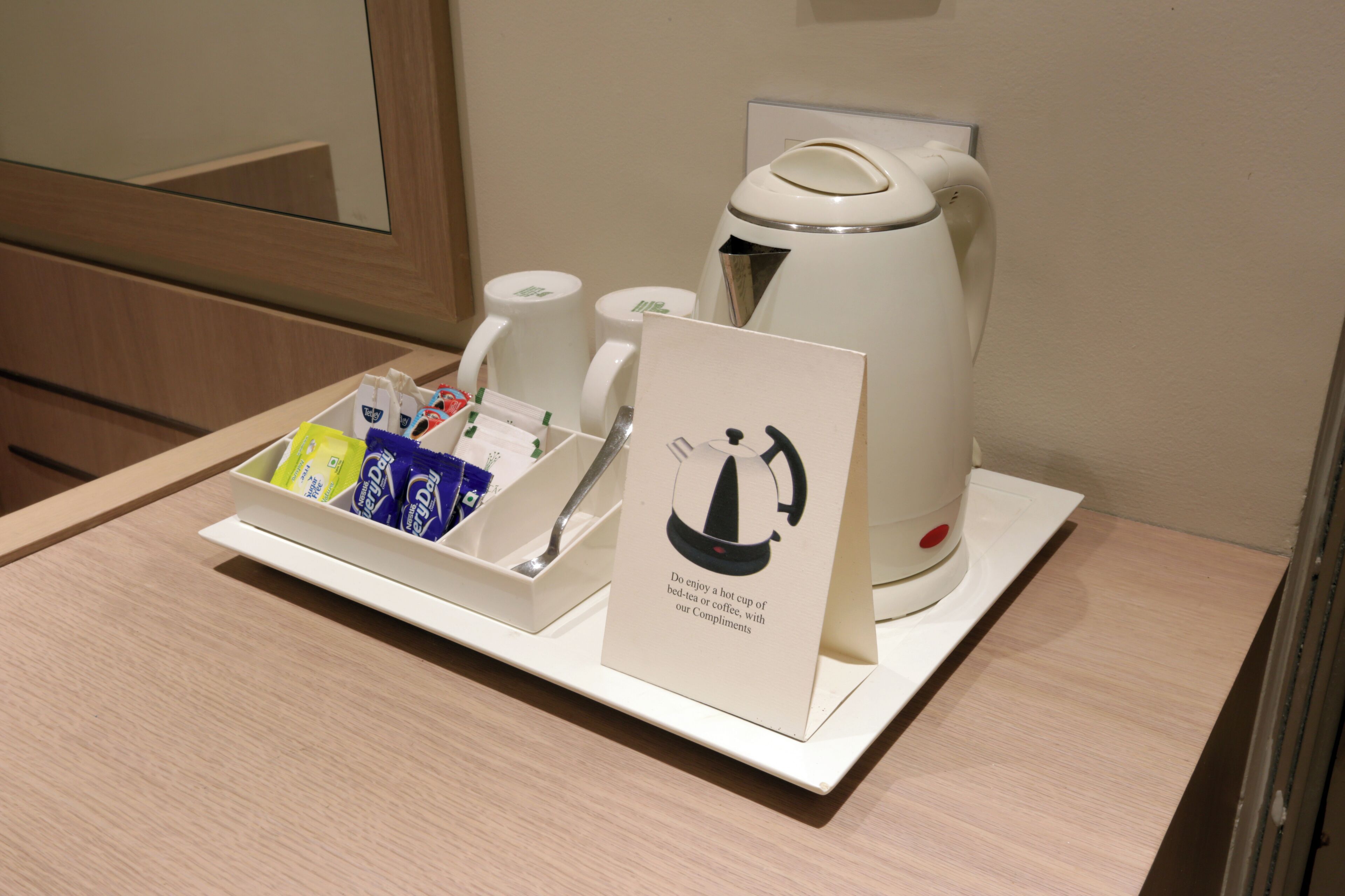 Ein Hotelzimmer mit Frühstücksaufstellung, inklusive Kaffeemaschine, Wasserkocher, Tassen und einem Tablett mit Frühstücksangeboten.