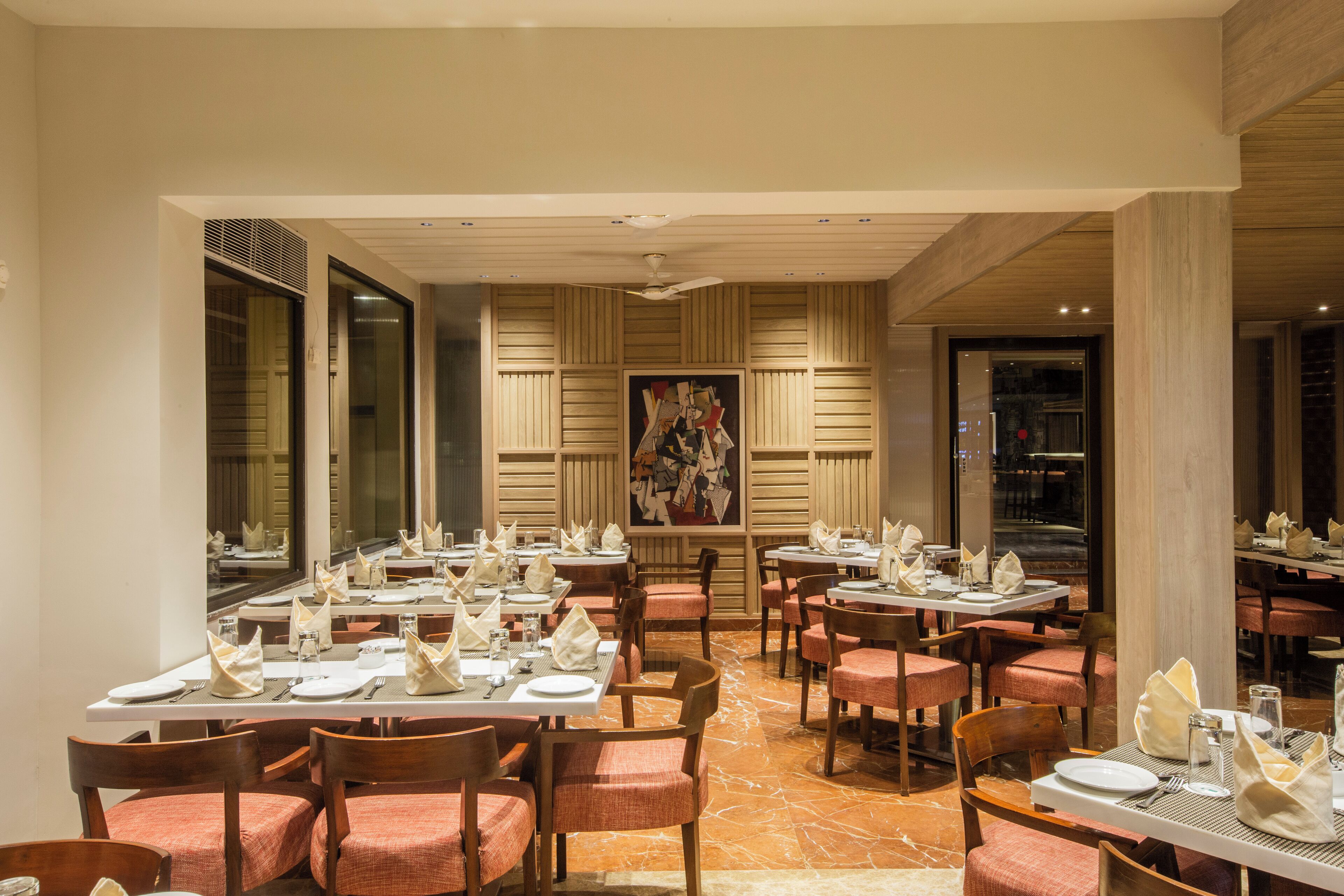 Un restaurant doté de nombreuses tables, recouvertes de nappes blanches, agrémentées de chaises à coussins rouges et où la décoration est soignée.