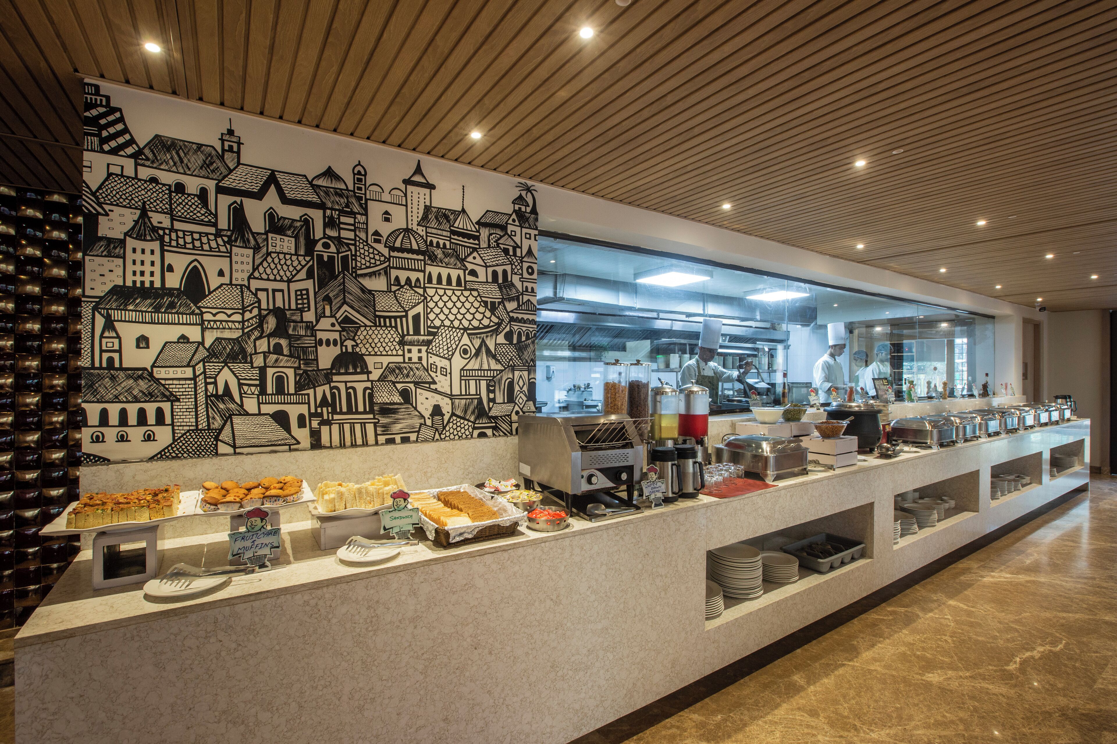A buffet setup with various food items and a cityscape mural on the wall.