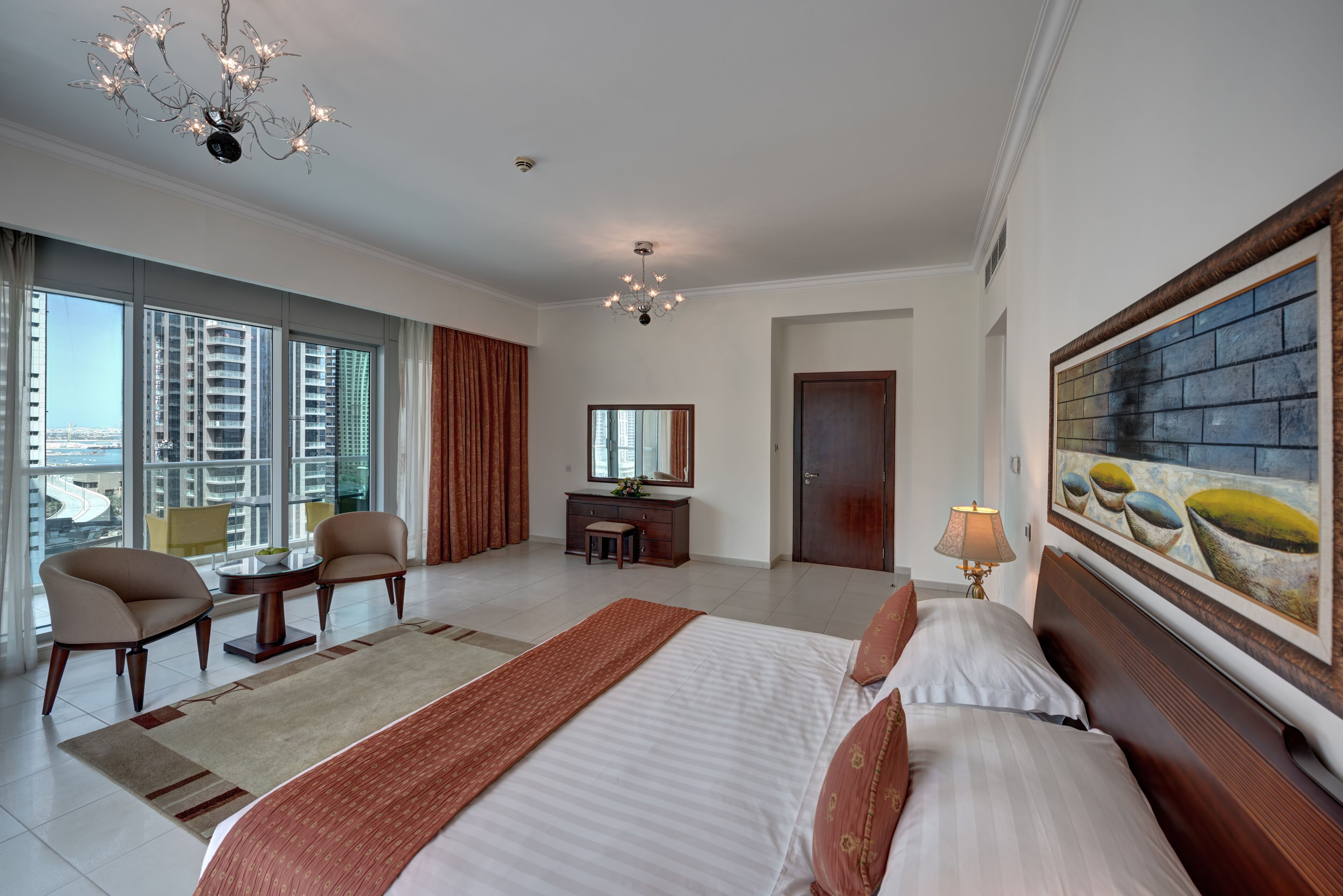 Een ruime hotelkamer met een groot bed, een zithoek met stoelen, een bureau en uitzicht op de stad door grote ramen.